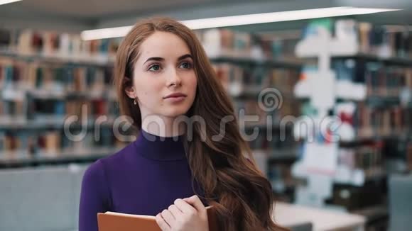 体贴的女孩站在图书馆里拿着一本书视频的预览图