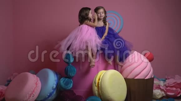 穿着连衣裙的赤脚女孩坐在装饰糖果之间互相讲述秘密慢动作视频的预览图