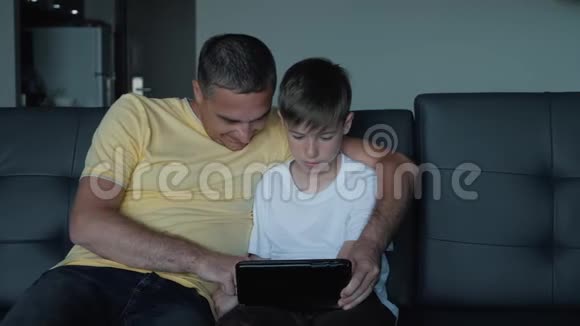父子俩坐在沙发上看电影在平板电脑上玩游戏一个幸福的家庭视频的预览图