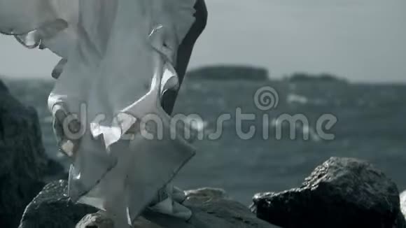 穿着白色裙子的新娘站在海洋上手里拿着一束花肮脏的白布随风飘扬水滴飞溅视频的预览图