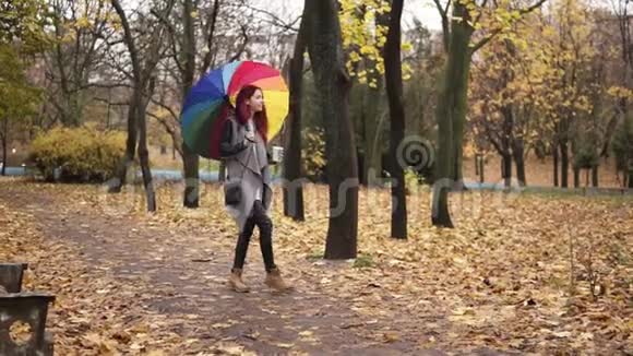 年轻时尚的女人一头红发在秋天公园散步一边拿着五颜六色的纸杯喝咖啡视频的预览图