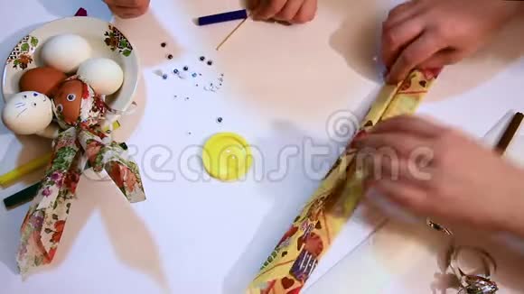 一个女孩的手的特写用彩色餐巾和闪亮的丝带装饰一个白色的鸡蛋有趣的面孔装修视频的预览图