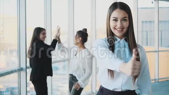 一位英俊年轻开朗微笑的商务女性在同事的背景下展示手势课视频的预览图