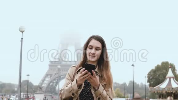 法国巴黎埃菲尔铁塔附近站在雾蒙蒙的早晨使用智能手机的年轻美女肖像视频的预览图
