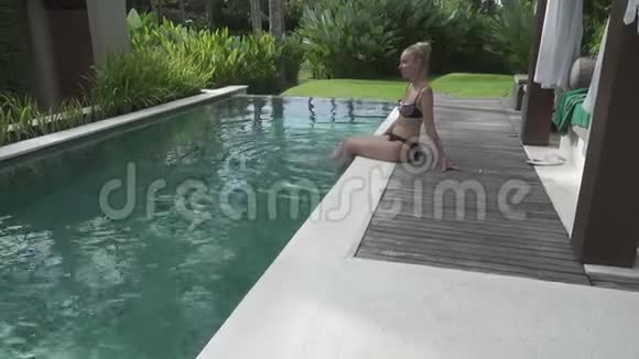 这位留着长发的年轻苗条女子在游泳池休息在热带度假胜地喝椰子鸡尾酒视频的预览图