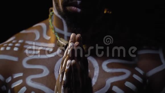 戴着白色仪式图案和项链的平安巴布亚人在黑暗中缓慢地祈祷视频的预览图