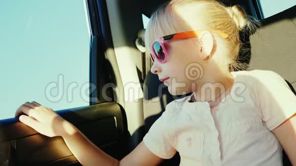 一个6岁的女孩戴着防晒的粉红色眼镜正坐在汽车的后座上用安全带系好视频的预览图