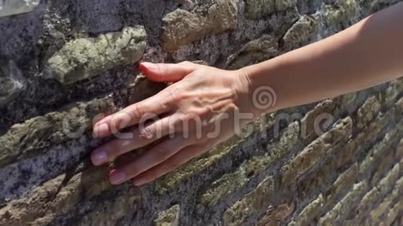 女人用手慢慢地靠在旧红砖墙上女性手摸石头粗糙表面视频的预览图