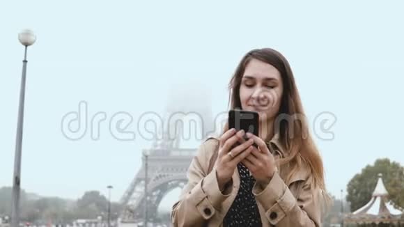 法国巴黎埃菲尔铁塔附近年轻时尚女性的肖像在雾天使用智能手机视频的预览图