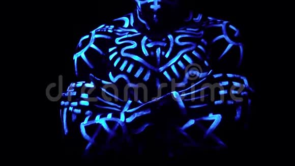 一个穿着霓虹灯图案的野蛮黑人把双臂交叉在胸前站在黑色背景的紫外线下视频的预览图