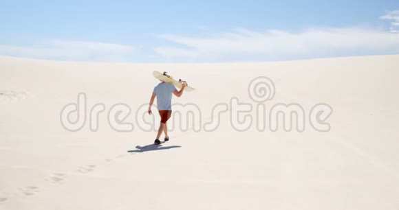 阳光明媚的一天一个带着沙板的人在沙漠中行走视频的预览图