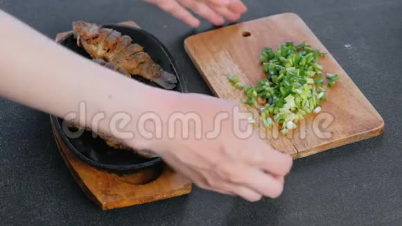 女人在黑桌上的厨房里端着一盘鱼和葱特写双手视频的预览图