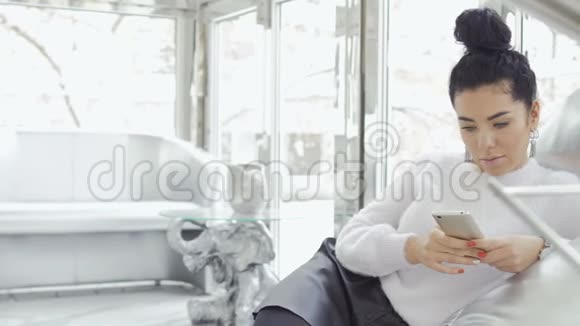 漂亮的黑发女人用手机放松扶手椅视频的预览图