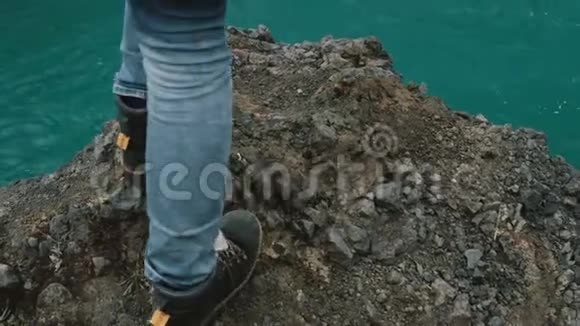 年轻的女人站在冰岛一个强大的瀑布附近的岩石上看着落水的水流视频的预览图
