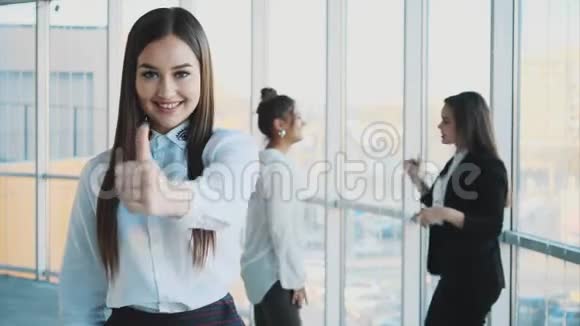 一位英俊年轻开朗微笑的商务女性在同事的背景下展示手势课视频的预览图