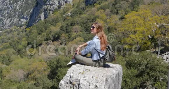 年轻的女旅行者坐在岩石上视频的预览图