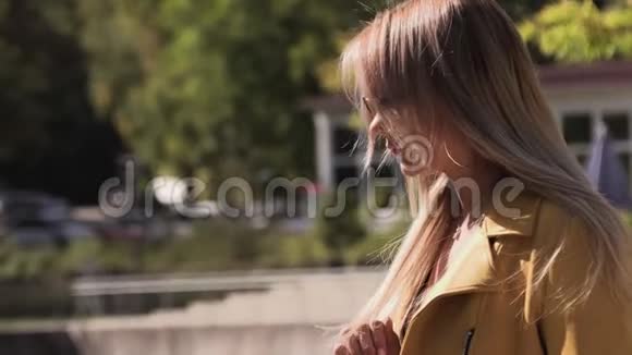 美丽的金发碧眼穿着黄色的夹克黑色的连衣裙和湖边的太阳镜视频的预览图