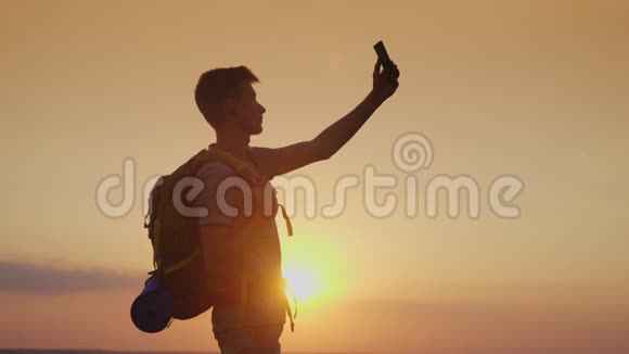一个带背包的少年用手机给自己拍照在夕阳下旅游和旅游视频的预览图