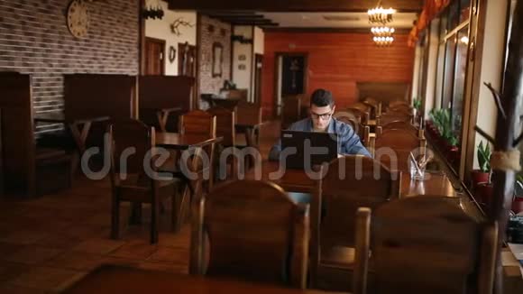 英俊的自由职业者商人戴眼镜勤奋地在咖啡馆的笔记本电脑上工作男子键盘打字和搜索新视频的预览图