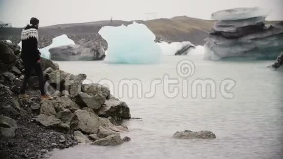 年轻英俊的男人在冰湖里散步快乐的游客坐在岩石上看着冰岛的冰川视频的预览图