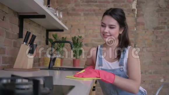 幸福的年轻女性家庭主妇戴着橡胶手套清洁厨房的灰尘家具视频的预览图