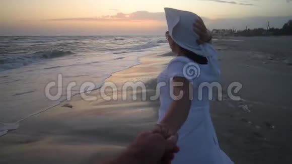 年轻漂亮的女人在日落时走在海边穿着白色连衣裙和白色帽子3她手里拿着相机跑开了视频的预览图