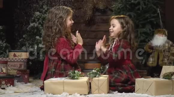 穿着裙子的快乐姐妹们拍手坐在房间里的圣诞礼物中雪正在下视频的预览图