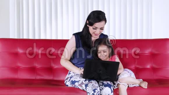 母亲和女儿用笔记本电脑在红色沙发上视频的预览图