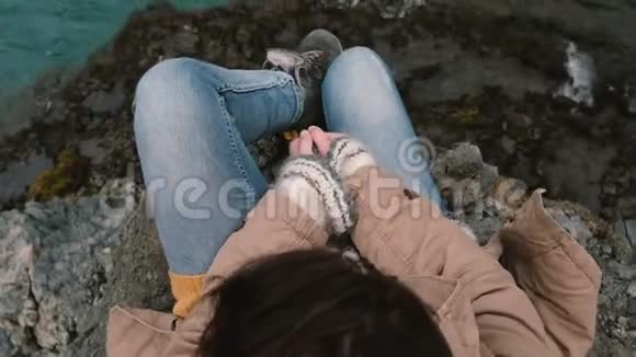 近景的年轻女子坐在靠近蓝水的岩石上独自徒步旅行的女性休息视频的预览图