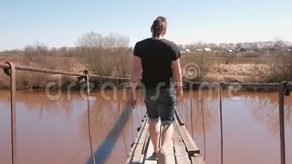 年轻人正走在河上一座悬挂的木桥上后景视频的预览图