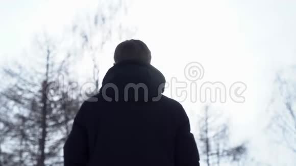 后景的人穿着温暖的夹克站立看着树木和灰色明亮的天空男性呼吸的后视图视频的预览图