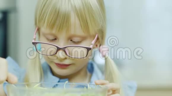 一个带眼镜的金发女孩的肖像吃一个大玻璃碗里的沙拉健康饮食视频的预览图