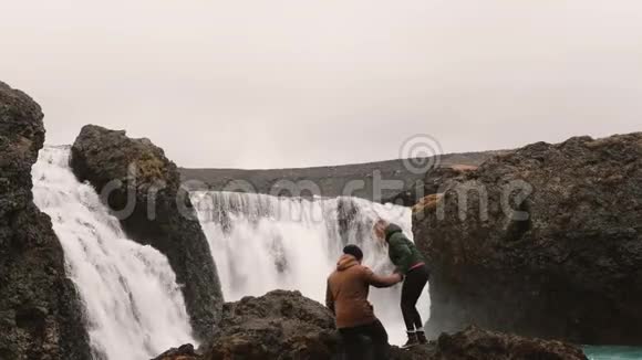 年轻的幸福夫妇一起徒步旅行看看冰岛有一个强大的瀑布男人和女人举起双手视频的预览图