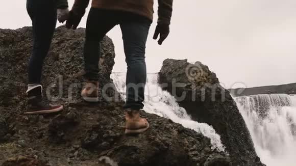 年轻的男人和女人站在山上后徒步旅行和看一个强大的瀑布在冰岛著名的景象视频的预览图