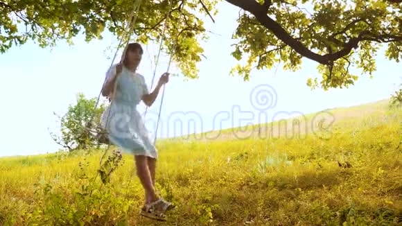一个美丽的女孩长发在一个夏天的橡树下摇摆穿着一件白色的连衣裙视频的预览图