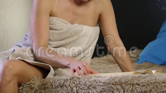 迷人的女人穿着浴巾看书美丽的年轻女孩舒适地躺在床上慢动作视频的预览图