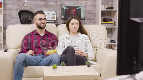 可爱的年轻夫妇坐在沙发上看电视视频的预览图