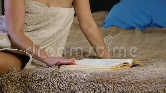 迷人的女人穿着浴巾看书美丽的年轻女孩舒适地躺在床上慢动作视频的预览图