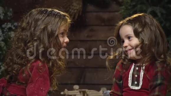 两个可爱的姐妹穿着衣服坐在落雪下的房间里穿着圣诞装饰品慢动作视频的预览图