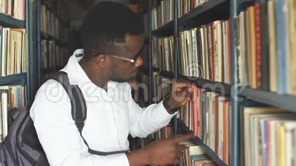 年轻的男学生在图书馆的书架间挑选书视频的预览图