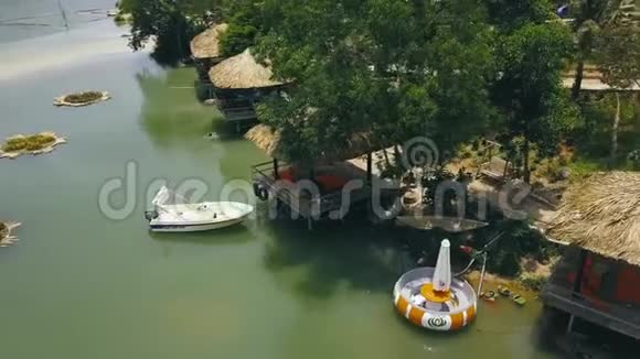 夏季平房与茅草屋顶和船在绿湖在水别墅度假无人机景绿色游泳的人视频的预览图