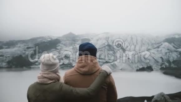 年轻夫妇站在冰湖的后景旅行男女一起探索冰岛视频的预览图