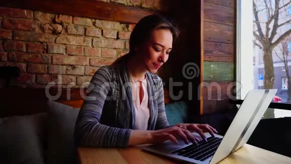 开朗的女性在咖啡馆用笔记本电脑给朋友打字微笑视频的预览图