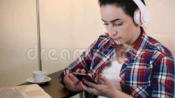 美女在耳机上听音乐在智能手机上打字视频的预览图