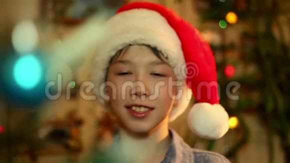 一个十几岁的男孩戴着圣诞老人的帽子在房子里装饰了一棵树视频的预览图