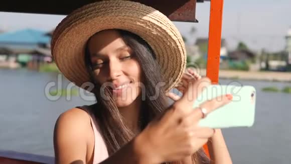 年轻快乐混血旅游妇女漂浮在木制泰国船和自拍照片使用手机泰国视频的预览图