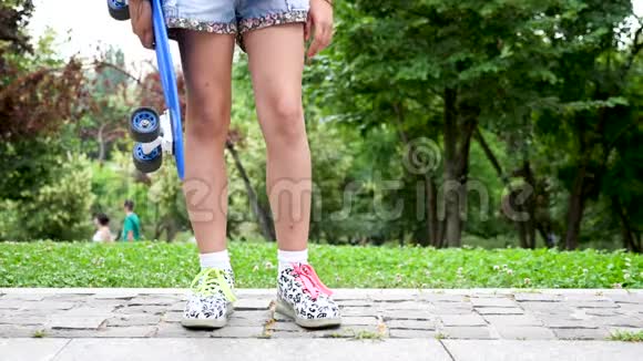 在公园里小女孩双脚合拢手里拿着一只蓝色的溜冰鞋视频的预览图
