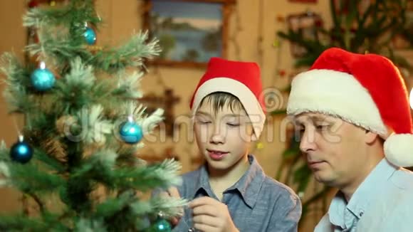 年轻快乐的父子戴着圣诞老人的帽子把圣诞树装饰进家门视频的预览图
