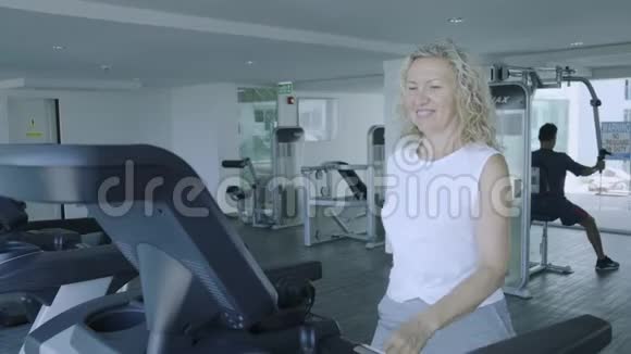 老年妇女在跑步机上健身房听音乐带耳机特写视频的预览图