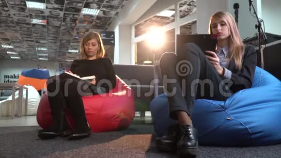 两个穿西装的女人把一些东西写在笔记本和平板电脑上和别人讨论视频的预览图